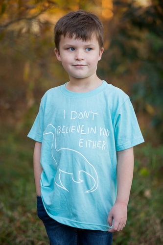 Boy wearing a teal shirt with white Nessy I don't believe in you either imprint.