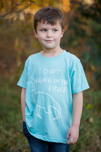 Boy wearing a teal shirt with white Nessy I don't believe in you either imprint.