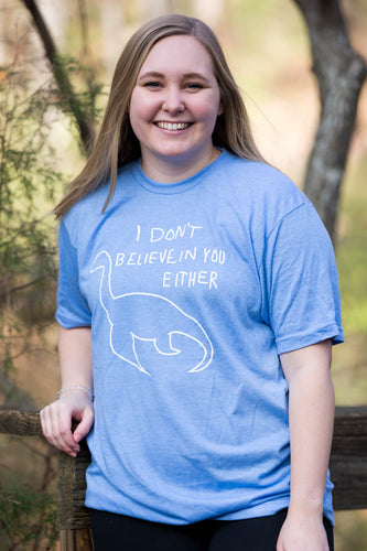 Woman wearing a blue shirt with white Nessy I don't believe in you either imprint.